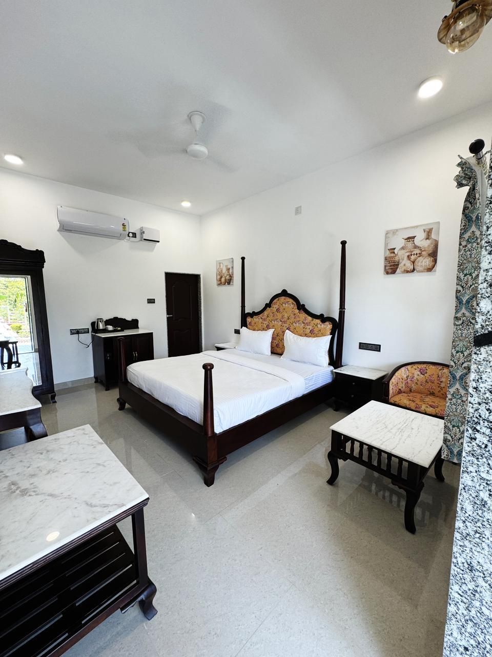 A bedroom with a bed, bedside tables, a chair, a desk, and an air conditioning unit.
