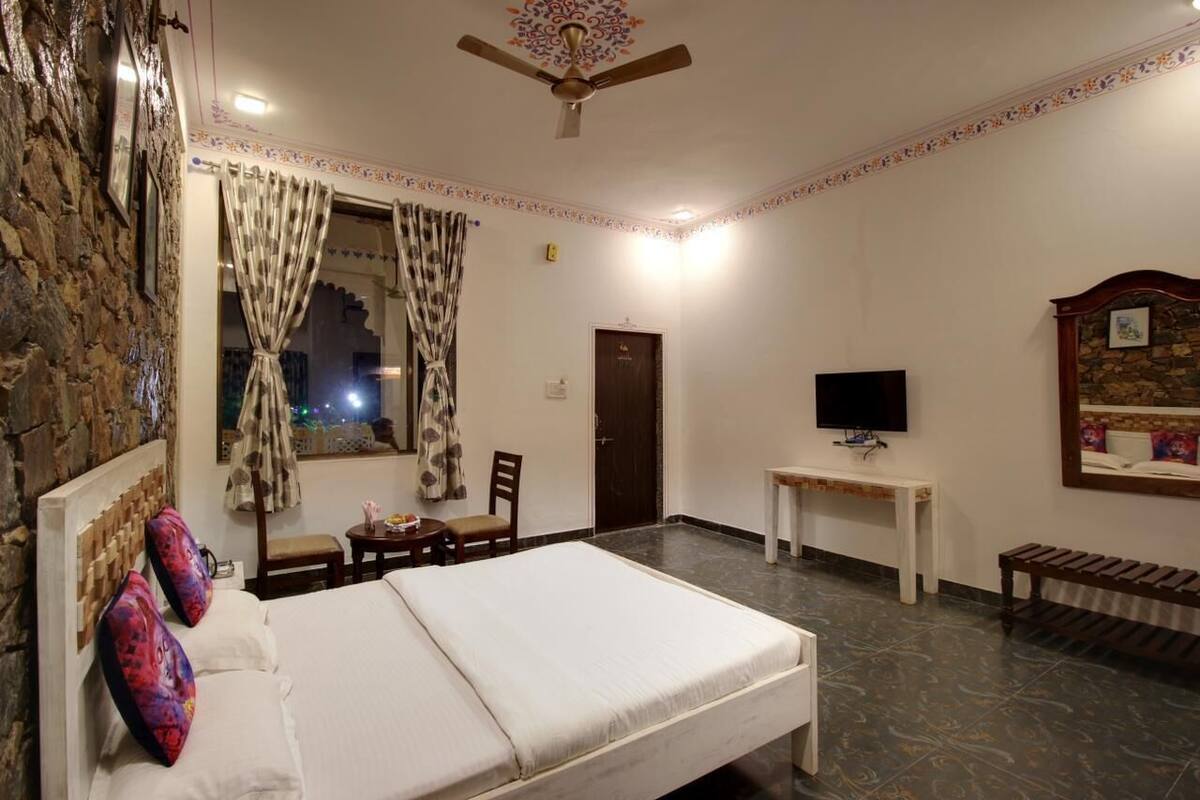 A hotel room with a bed, a TV, a small table, and a bench.