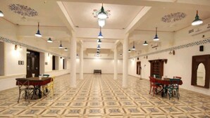 A spacious hall with patterned flooring, multiple tables, and hanging lights. - Yash Veer Resort (Sirohi)