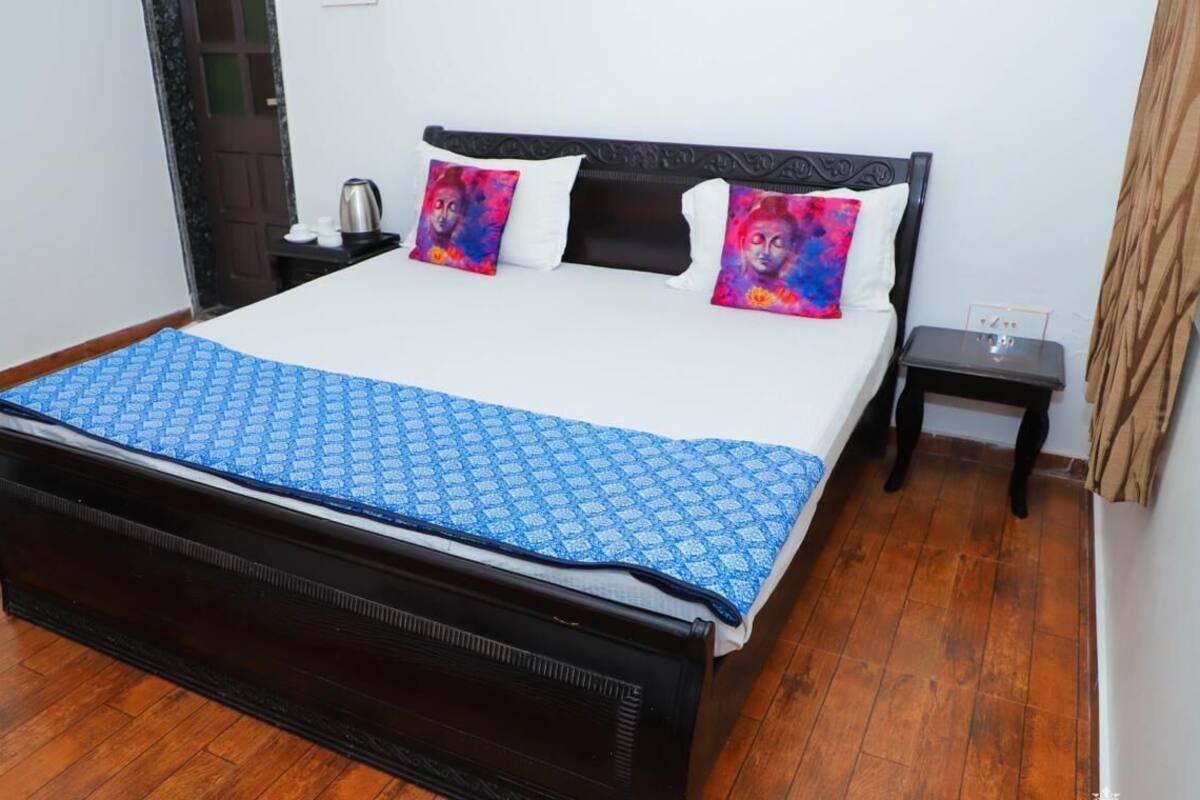 A bed with a patterned bedspread, two pillows with colorful artwork, a bedside table with a lamp, and a wooden floor.
