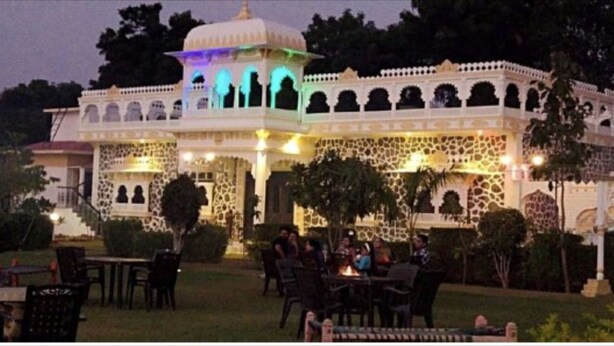 A traditional building with a central dome and multiple arches, surrounded by a well-maintained garden with outdoor seating. - Yash Veer Resort (Sirohi)