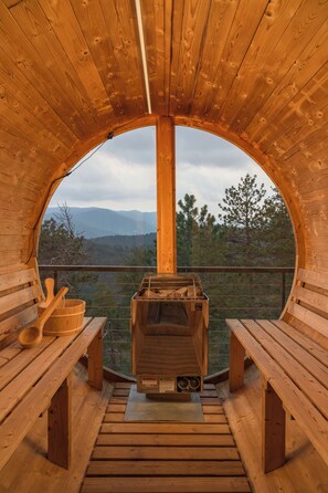 Une cabane en bois dotée d’une grande fenêtre circulaire qui offre une vue sur les montagnes et les arbres.