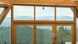 Une fenêtre à cadre en bois donnant sur une forêt et des montagnes.