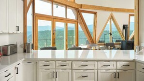 Une cuisine moderne avec de grandes fenêtres, des poutres en bois et une vue sur les montagnes.