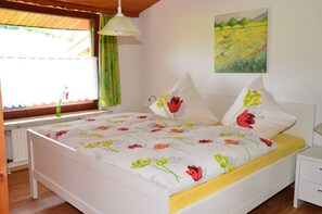 A bedroom with a bed, a nightstand, a window with curtains, a painting on the wall, and a radiator. - Apartment '2, 45qm' with Private Terrace, Private Garden and Wi-Fi (Herscheid)