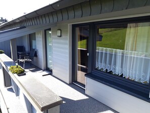 A building with a covered outdoor seating area, a door with a curtain, and a window with a view of the outdoors. - Apartment '2, 45qm' with Private Terrace, Private Garden and Wi-Fi (Herscheid)