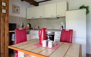 A kitchen with white cabinets, a red table, and a red chair. - Apartment '2, 45qm' with Private Terrace, Private Garden and Wi-Fi (Herscheid)