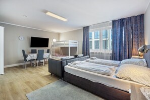 Un dormitorio con una cama alta, un escritorio con silla, un televisor y una ventana con cortinas.