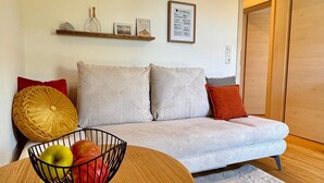 A living room with a sofa, a round wooden table with a fruit bowl, a fluffy rug, and a wooden door. - Holiday Apartment "Kathi‘s Allgäuliebe" with Mountain View, Private Terrace & Wi-Fi (Weitnau)