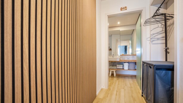A hallway with a wooden slat wall, a sink area with a mirror, and a black cabinet. - Holiday Apartment "Kathi‘s Allgäuliebe" with Mountain View, Private Terrace & Wi-Fi (Weitnau)