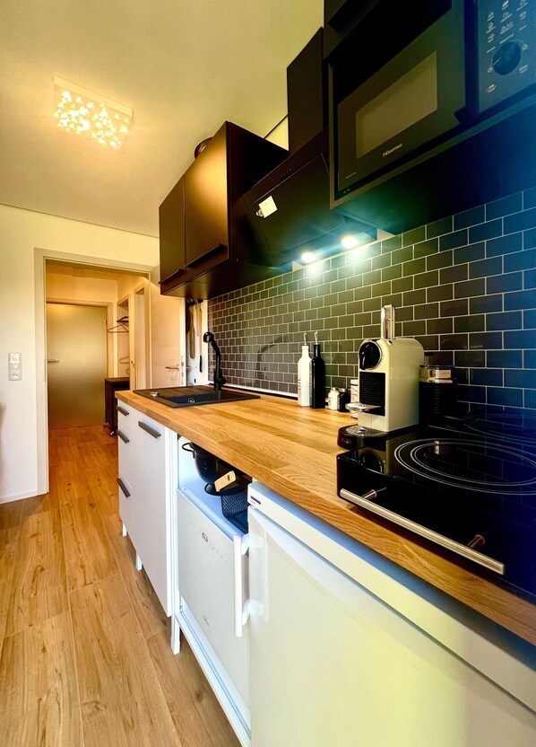 A kitchen with a wooden countertop, black appliances, and a tiled backsplash.