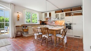 Une cuisine avec une table à manger, des chaises, une fenêtre et un sol carrelé.