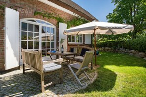 Une terrasse extérieure avec une table et des chaises, un grand parasol et un bâtiment en briques doté d’une fenêtre.