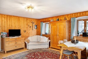 Ein Zimmer mit Holzwänden, einer Couch, einem Fernseher, einem Esstisch und einem gemusterten Teppich.