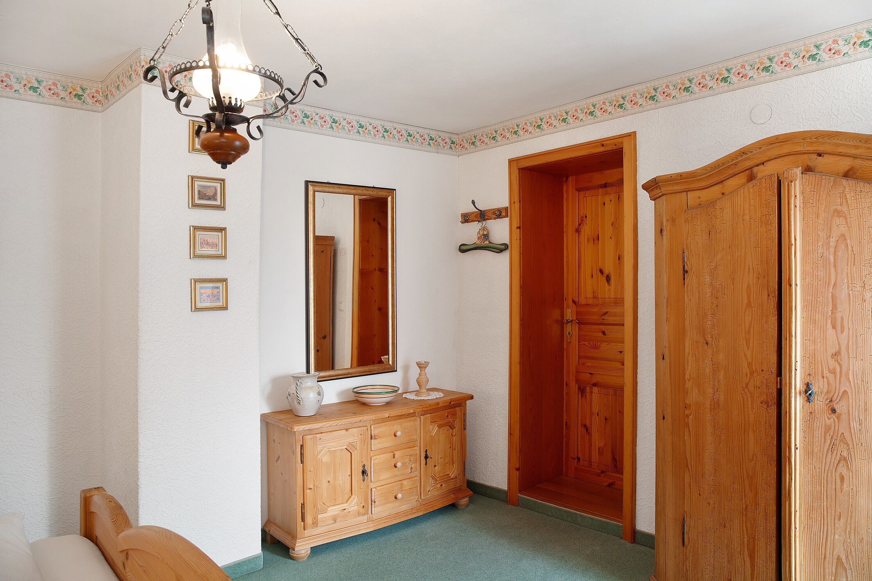 Une pièce comprenant une commode en bois, un miroir, un lustre et une armoire en bois.