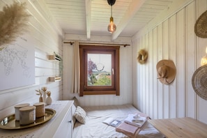 Un dormitorio con techo de madera, ventana con vistas, cama con almohadas, mesita de noche y perchero en la pared.
