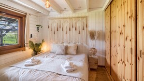 A bedroom with a bed, a window, a plant, a macrame wall hanging, and wooden walls.