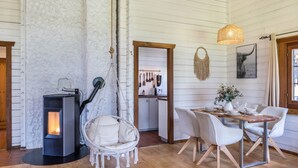 A cozy interior with a wood-burning stove, a hanging chair, a dining table with chairs, and a kitchen area.