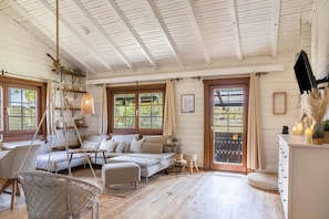 Una habitación acogedora con sofá, sillón colgante, zona de comedor y un amplio ventanal con vistas.