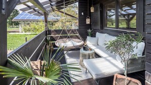 A covered outdoor seating area with a sofa, a hanging chair, and potted plants.