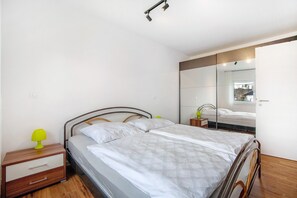 A bedroom with a bed, a nightstand, a mirror, and a wooden floor.