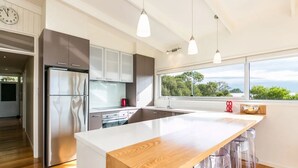 Een moderne keuken met een groot eiland, roestvrijstalen apparatuur en uitzicht op groen buiten het raam.