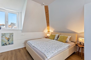 A bedroom with a bed, a nightstand, a lamp, a painting, and a window.