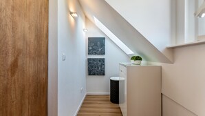 Un couloir étroit avec un plancher en bois, des murs blancs, une poubelle noire, une armoire blanche et une petite plante en pot.