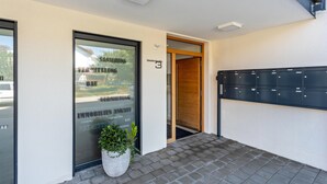 Une entrée moderne avec une porte en verre, une plante en pot et une rangée de boîtes aux lettres noires.