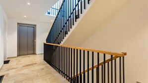 Un escalier moderne avec une main courante en bois et des balustres noires, menant à un ascenseur.