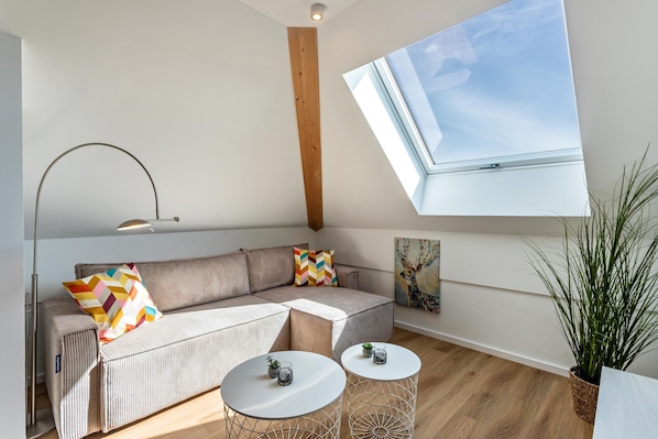 A modern living room with a sectional sofa, two round tables, a skylight, and a large window.
