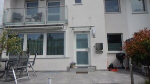 A two-story building with a balcony, a door with a number plate, and a barbecue grill in the yard. - Holiday Home 'Viktoria' with Private Terrace, Garden, and Wi-Fi (Koblenz)