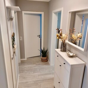 A hallway with a white door, a potted plant, a dresser with drawers, and a mirror. - Apartment 'Am Hochwald' with Mountain View, Private Terrace and Wi-Fi (Reinhardtsdorf-Schöna)