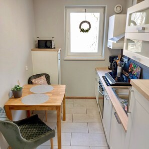 Kompakti keittiö, jossa on ruokapöytä, mikroaaltouuni hyllyllä, kahvinkeitin ja ikkuna, josta on näkymä.