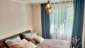 Ein Schlafzimmer mit einem Bett, Nachttischen, einer Lampe und einem Fenster mit Vorhängen.