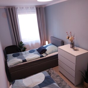 A bedroom with a bed, a bedside table, a dresser, a window with curtains, and a plant. - Apartment 'Am Hochwald' with Mountain View, Private Terrace and Wi-Fi (Reinhardtsdorf-Schöna)