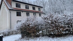 Ein zweistöckiges Gebäude mit geneigtem Dach, umgeben von schneebedeckten Bäumen und Sträuchern.