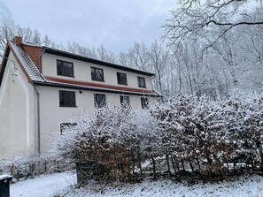 Ein zweistöckiges Gebäude mit geneigtem Dach, umgeben von schneebedeckten Bäumen und Sträuchern.