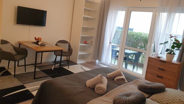 Une chambre à coucher comprenant un lit, un bureau, des chaises, une télévision, un balcon avec vue et une plante en pot.