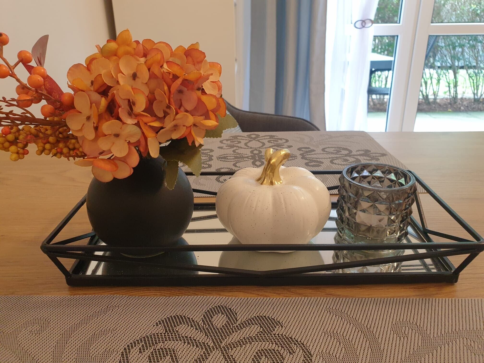A table with a vase of flowers, a white pumpkin, and a glass candle holder.