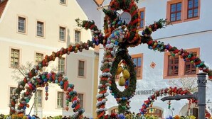 Une structure en pierre agrémentée de décorations colorées, notamment une guirlande et des ornements sphériques, située dans un environnement urbain.