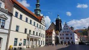 Une place historique au cœur d’une ville européenne, caractérisée par son architecture traditionnelle, notamment une imposante tour de l’horloge et une église surmontée d’une flèche.
