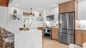 A modern kitchen with white cabinetry, stainless steel appliances, and a marble island. - Hot tub, 290 Wine Trail, Covered Pavilion! (Fredericksburg)