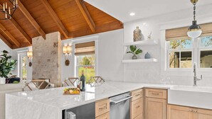 A modern kitchen with a marble island, wooden cabinets, and a stone accent wall. - Hot tub, 290 Wine Trail, Covered Pavilion! (Fredericksburg)