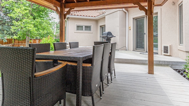 Un patio techado con techo de madera, un juego de comedor exterior y una vista de una casa al fondo.
