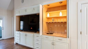 Una cocina con armarios blancos, horno empotrado y una estantería para vinos con copas.