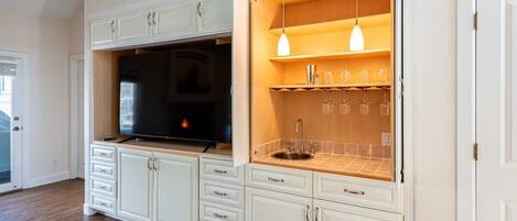 Una cocina con armarios blancos, horno empotrado y una estantería para vinos con copas.