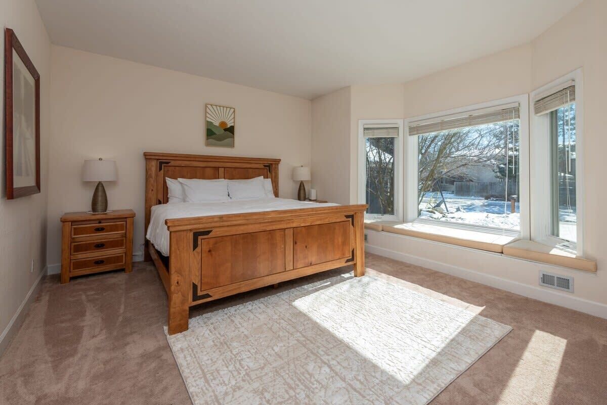 A bedroom with a wooden bed, bedside tables, a window with a view of trees, and a framed picture on the wall.