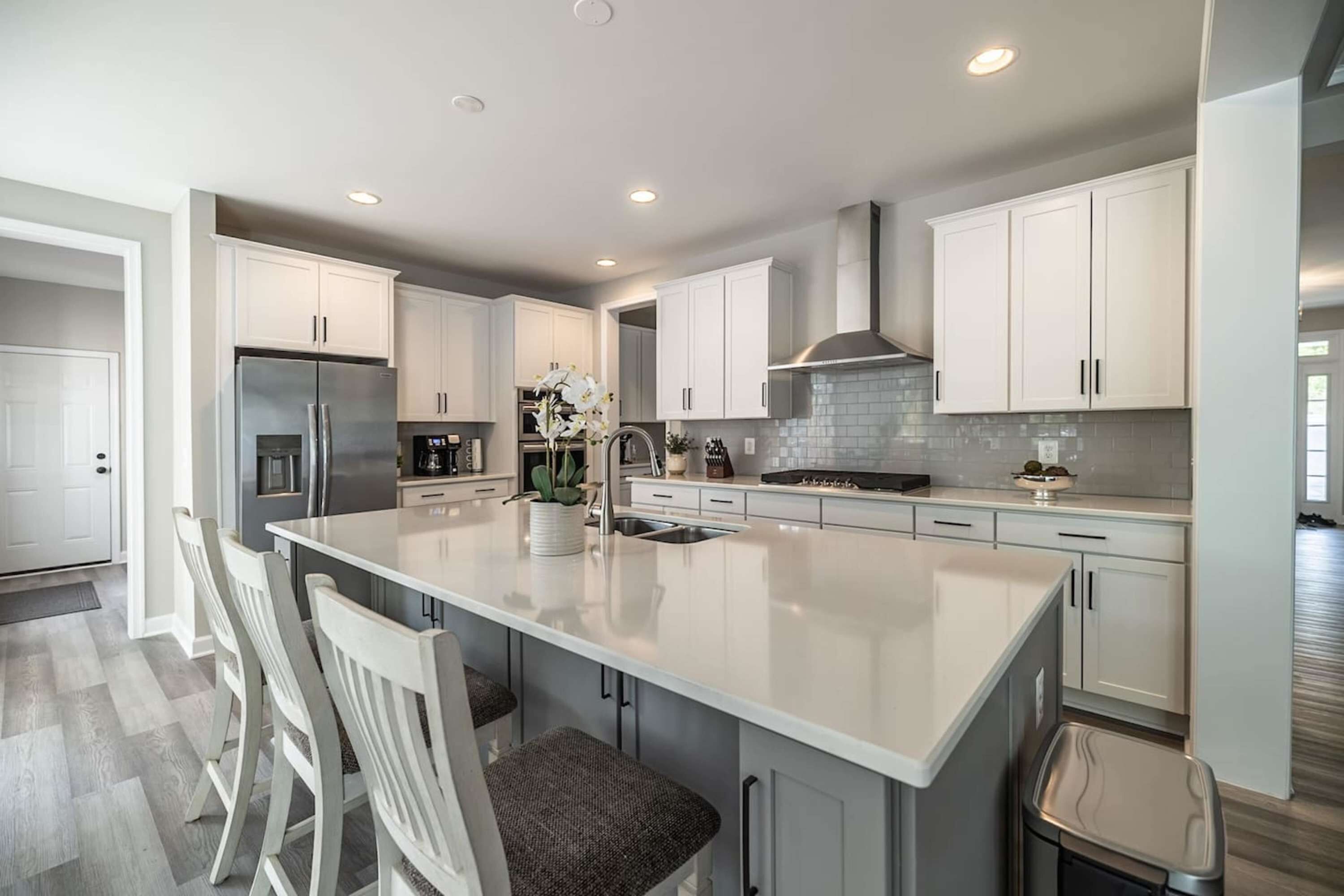 Una cocina moderna con armarios blancos, un refrigerador de acero inoxidable y una isla central con taburetes de bar.