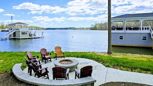 A lakeside deck with Adirondack chairs, a fire pit, and a view of a docked boat. - Private Paradise 2 Story Dock, Beach, Hot Tub (Mineral)